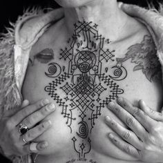 a woman with tattoos on her chest is holding her hands in front of her chest