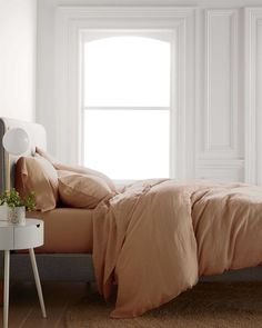 a bedroom with a bed, nightstand and window in front of white walls that has light shining through the windows