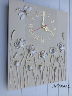 a white clock with flowers and dragonflies on the face is mounted to a wall