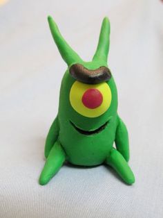 a green toy sitting on top of a white bed next to a red and yellow object