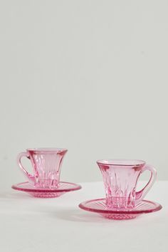 two pink glass cups and saucers sitting next to each other on a white surface