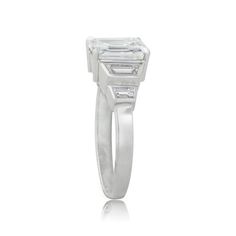 A beautiful Estate Emerald Cut Diamond Engagement Ring, accented by a tapered baguette and bullet-cut diamonds on either side. Timeless Three Stone Emerald Ring For Formal Occasions, Platinum Emerald Cut Three Stone Ring, Three-stone Octagon Diamond Ring, Three Stone Diamond Ring, Octagon Shaped, Diamond Three-stone Ring With Octagon Shape, Three Stone Emerald Cut Diamond Ring In Diamond White, Modern Emerald Baguette Cut Ring, Platinum Emerald Cut Ring With Bezel Setting, Modern Emerald Ring With Vvs Clarity And Baguette Cut