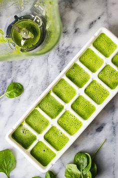 an ice tray filled with green liquid next to basil leaves