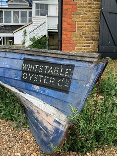 an old blue boat sitting on top of a gravel field next to a building with a sign that reads, whisstable oyster co