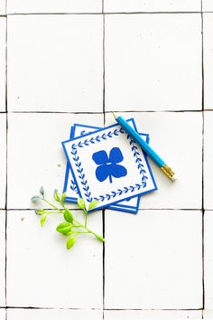 two blue coasters with four leaf designs on them and a pen resting on one