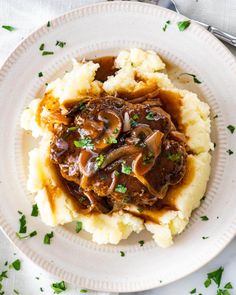 a white plate topped with mashed potatoes covered in gravy and mushrooms on top