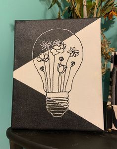 a black and white painting with flowers in a lightbulb on the side of a table