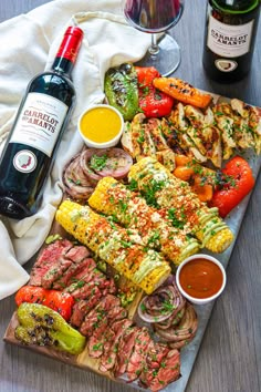 an assortment of meats and vegetables on a platter next to two bottles of wine