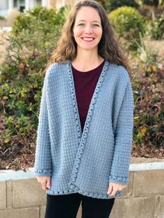 a woman standing in front of a brick wall wearing a blue sweater and black pants