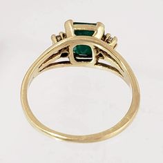 "This magnificent vintage ring boasts a lovely emerald and two diamonds set in 18K yellow gold. The emerald has a rich bluish-green color and weighs in at 1 1/4 carats. An accent diamond is set on each side of the emerald, adding elegance and sparkle. The ring has triple branched shoulders that add interest beyond the classic shank. Luxurious! Vintage: 1990s Size: 6 Materials: 18K Yellow Gold, Emerald, Diamonds Marked: 18K Emerald: 7 mm x 7mm x 4.4mm, approx. 1.25 ct. 2 Diamonds: brilliant cut, Gold Emerald Cut Hallmarked Emerald Ring, Gold Emerald Ring With Brilliant Cut, 14k Gold Emerald Ring With 17 Jewels - Collectible, Collectible Green Emerald Ring In 14k Gold, Collectible 14k Gold Emerald Ring, Green 14k Gold Emerald Ring Collectible, Vintage Style Emerald Cluster Ring In Yellow Gold, Gold Emerald Ring With Prong Setting In Heirloom Style, Fine Jewelry Yellow Gold Emerald Ring For Collectors