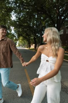 a man and woman holding hands while walking down the street with trees in the background