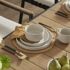 a wooden table topped with plates and bowls filled with pears next to white dishes