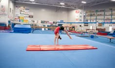 a person doing a handstand on top of a red mat in a gym