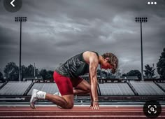 a man in red shorts and black shirt is running on a track with stadium lights behind him