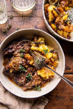 a bowl filled with meat and potatoes on top of a wooden table next to a glass of water