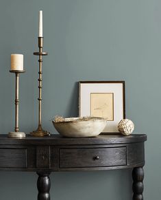 a wooden table topped with a bowl and two candles next to a framed photograph on the wall