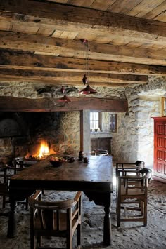 an old rustic dining room with stone walls and beams on the ceiling is lit by a fireplace