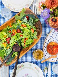 a table topped with plates and bowls filled with salad next to utensils on top of a blue checkered table cloth