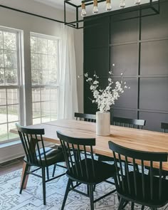 a dining room table with black chairs and white flowers in a vase on the table