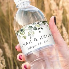 a person holding a bottle of water in front of some flowers and grass with the label on it