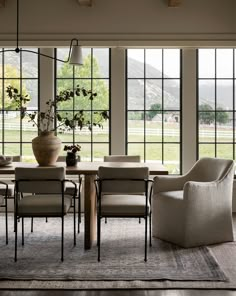 the dining room table is surrounded by chairs and vases with flowers in them, along with large windows that look out onto a grassy field