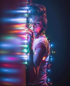 a woman standing in front of a wall with christmas lights on her face and arms