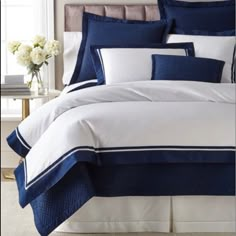 a bed with blue and white comforters in a bedroom next to a vase filled with flowers