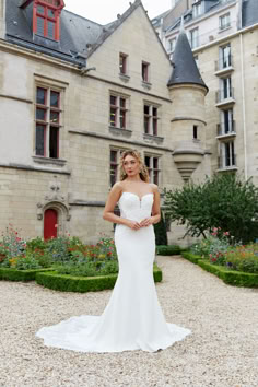 a woman standing in front of a building wearing a wedding dress and looking at the camera