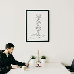 a man sitting at a table with a laptop in front of him and a drawing on the wall behind him