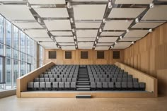 an empty auditorium with rows of seats in front of large windows and wooden flooring