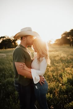 a man and woman standing together in a field at sunset with the sun behind them