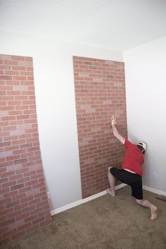 a man standing in front of a brick wall reaching up to grab something off the floor