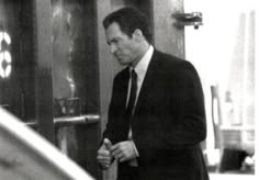 a man in a suit and tie walking out of a building with his hand on the door handle