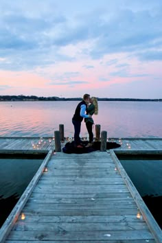 a man and woman kissing on a dock at dusk with candles in the water behind them