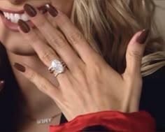 a close up of a person wearing a ring on their finger and holding her hand near her face