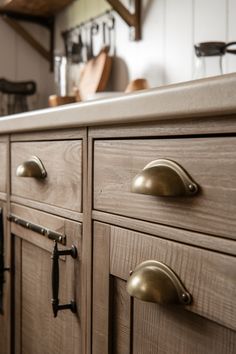 Wooden kitchen cabinets with bronze handles under a beige countertop. Farmhouse Hardware Kitchen, Farmhouse Drawer Pulls Kitchen, Farmhouse Kitchen Hardware For Cabinets, Farmhouse Kitchen Handles, Farmhouse Kitchen Cabinet Handles, Farmhouse Cabinet Hardware, Affordable Farmhouse Kitchen, Farmhouse Kitchen Hardware, Rustic Drawer Pulls