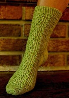 a woman's legs wearing green socks and holding her leg up against a brick wall