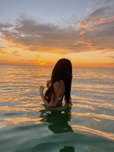 a woman is sitting in the water with her back to the camera and looking at the sunset