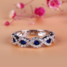 a white gold ring with blue sapphire stones and diamonds on the sides, surrounded by pink flowers