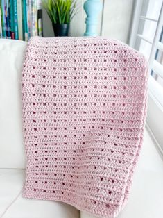 a pink crocheted blanket sitting on top of a white couch