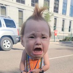 a toddler crying in the street with beads around his neck and hair sticking out