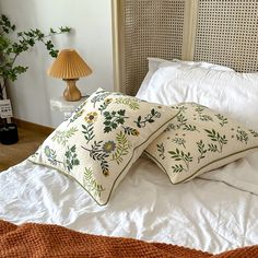 two pillows sitting on top of a white bed next to a night stand and lamp