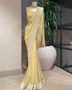 a yellow sari draped over a mannequin in front of a potted plant