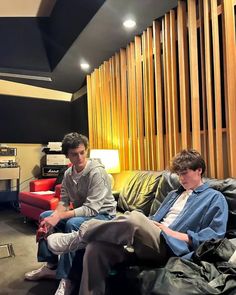 two young men sitting on top of couches in a living room next to each other