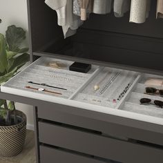 an open drawer containing jewelry and other items on the counter in front of a potted plant