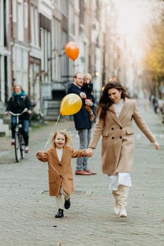 a woman and child holding hands while walking down the street with balloons in their hand