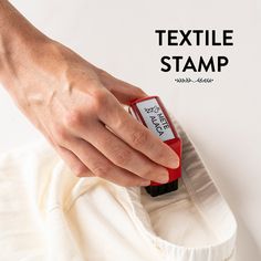 a hand is holding a red and black stamper over a white shirt with the text textile stamp on it