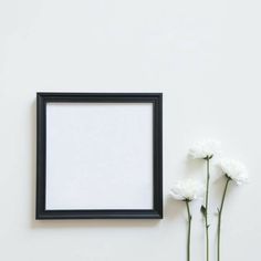 three white flowers are in front of a black frame on the wall next to it