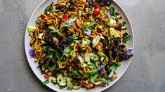 a white plate topped with noodles and veggies on top of a gray table