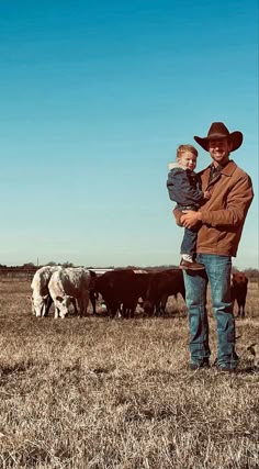 a man holding a small child in front of cattle